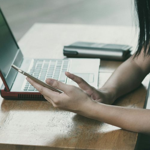 pexels-photo-363766-363766 A young woman multitasking with her smartphone and laptop at a table indoors.